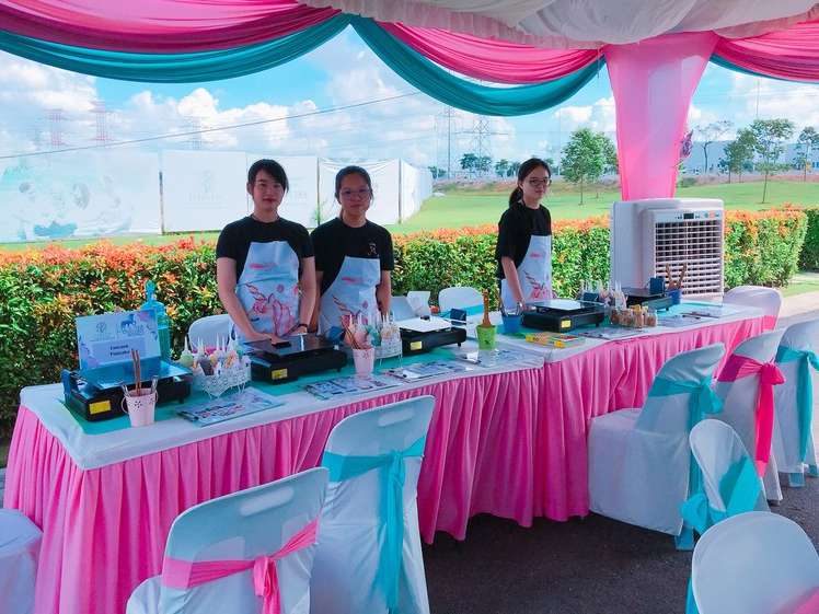 Crew members at a DIY food activity stall under pink and teal tent decorations