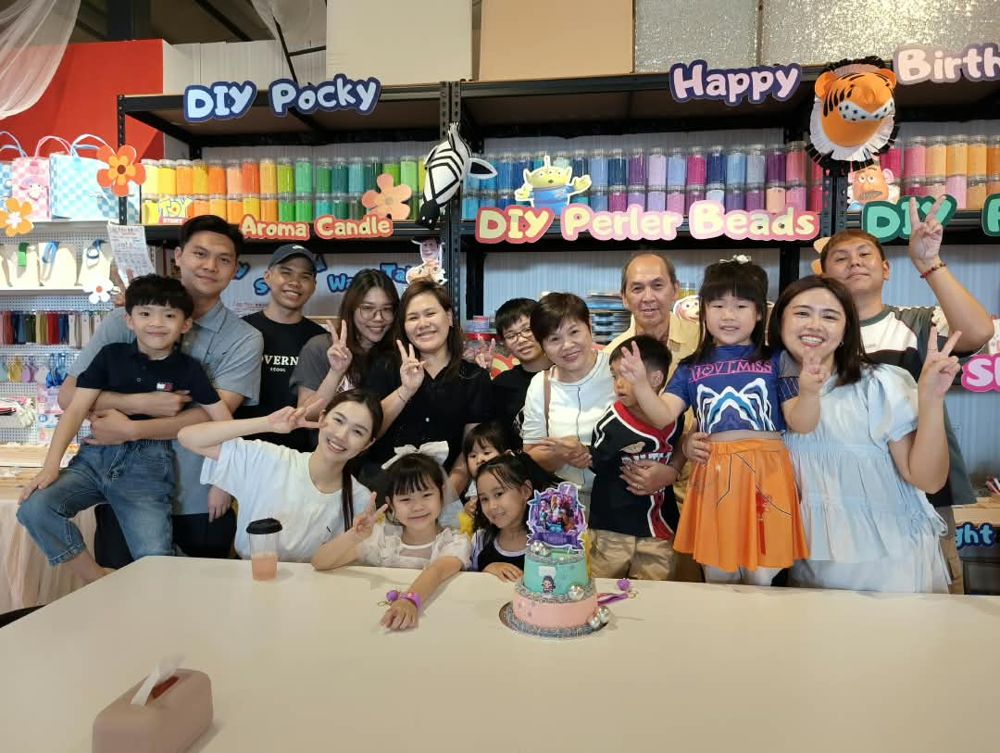 A group of children and adults smiling and making peace signs around a birthday cake at a DIY studio